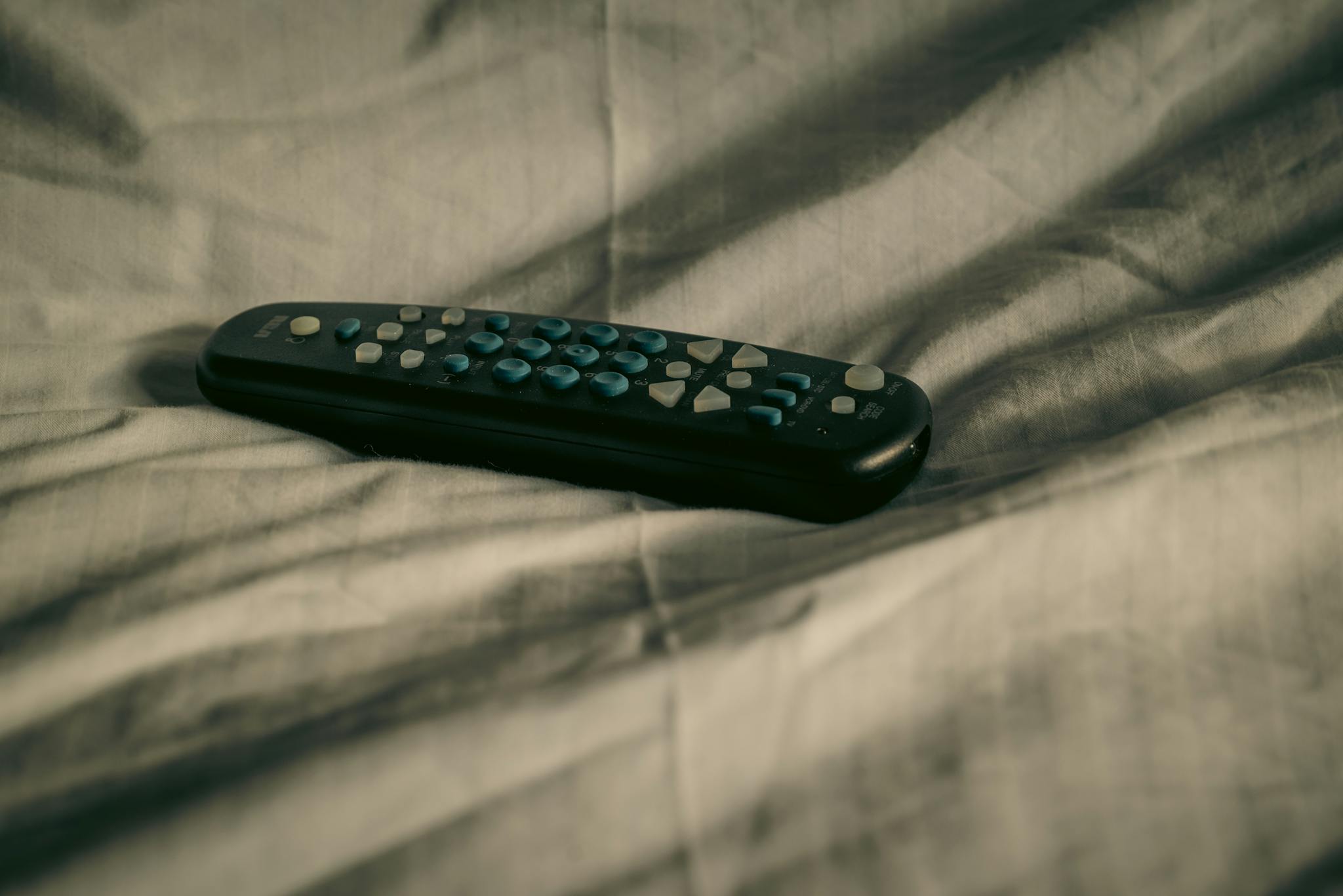 A remote control rests on wrinkled bed sheets, conveying a cozy and relaxed atmosphere.