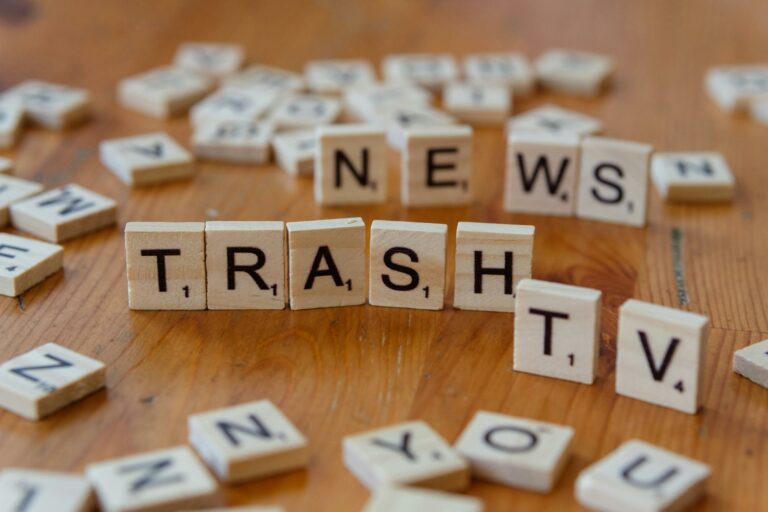 Close-up of wooden letter tiles spelling out Trash TV News on a table.