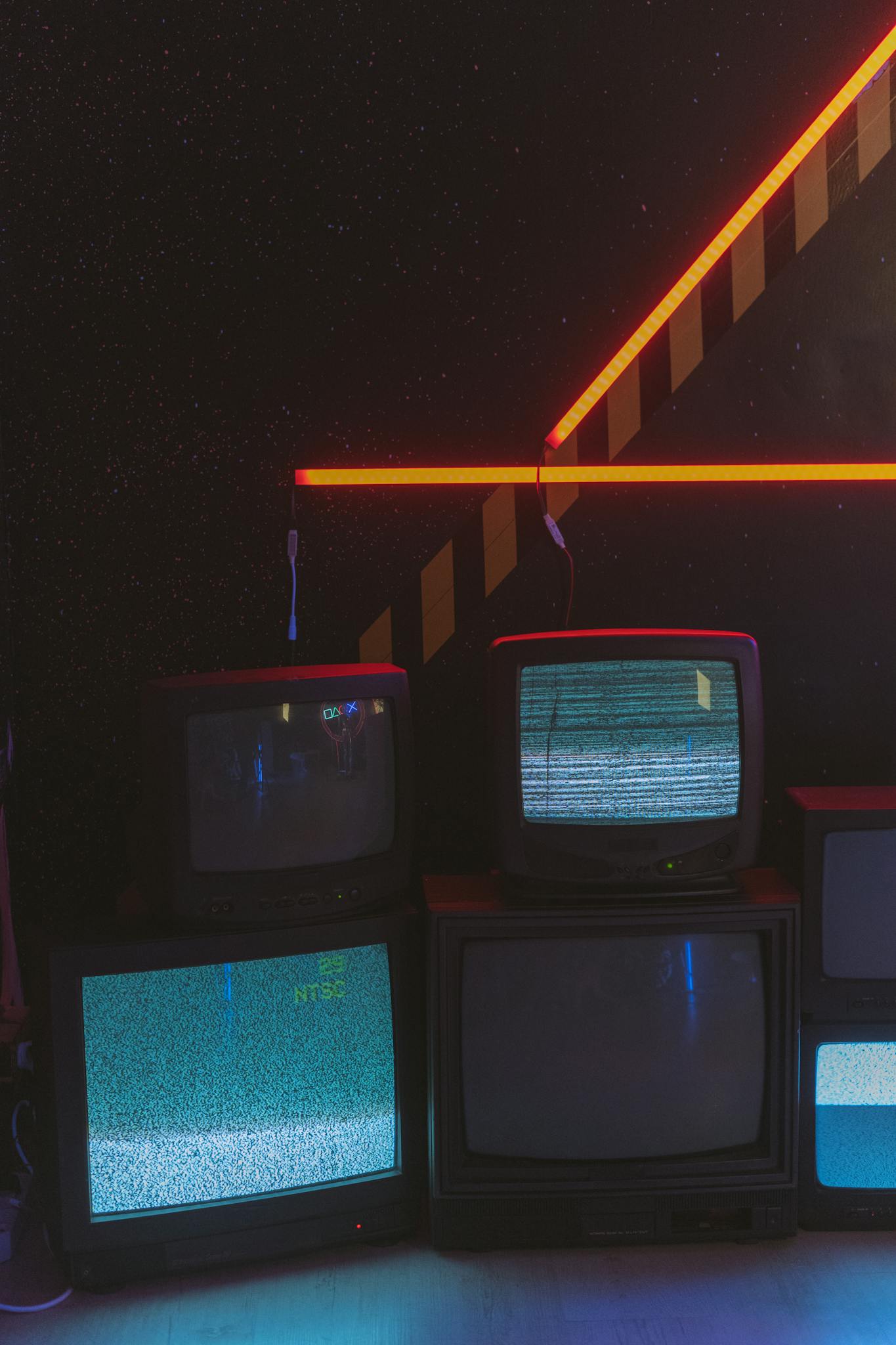 Vintage televisions display static in a dark room accented by bright neon lights.